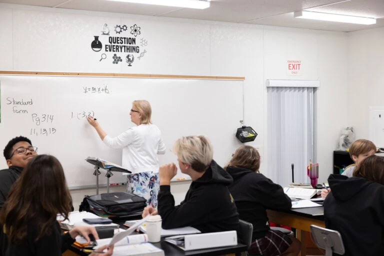 Students learning with teacher turned towards whiteboard.